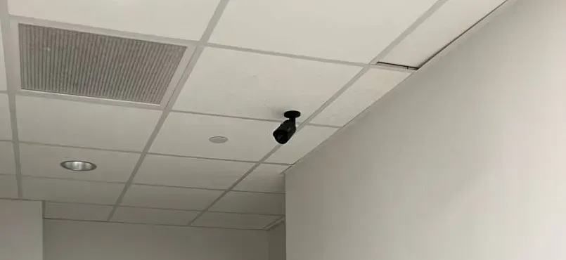 Black bullet camera beside a return-air grille — Nassau County Uniview installation example photo Black bullet camera beside a return-air grille and a downlight on a drop ceiling — Uniview camera installation Nassau County example