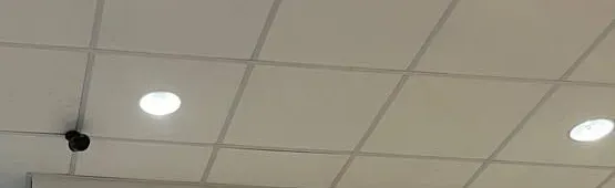 Small black camera on a ceiling grid near recessed lights — Uniview camera installation Nassau County example Small black camera on a white ceiling grid near two recessed lights — Nassau County Uniview camera installation example