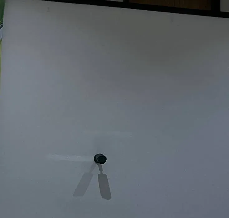 Small camera high on a plain wall casting two shadows — Uniview installation Nassau County example photo Small black camera high on a plain wall casting two shadows — Uniview camera installation Nassau County example