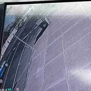 Wide-angle recorder view of sidewalk and curb — Staten Island Uniview driveway reference Staten Island Uniview curb-view reference photo: a monitor showing a wide-angle camera view of a paved sidewalk, a curb line and the edge of a parked car