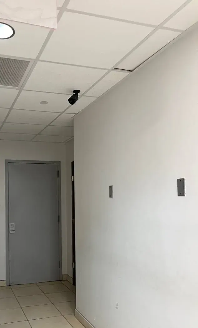 Video wall installation Long Island example photo: a plain white corridor wall with two small wall plates, a grey door and a camera at the drop ceiling