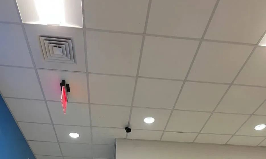Video wall installation Long Island example photo: an office drop ceiling with an air diffuser, a lit red exit sign, recessed lights and a small black camera