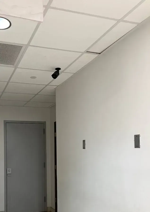 Blank corridor wall with two cover plates — Westchester wall-position reference Westchester County video wall reference photo: a plain white corridor wall with two metal cover plates, a grey door and a small camera at the ceiling line
