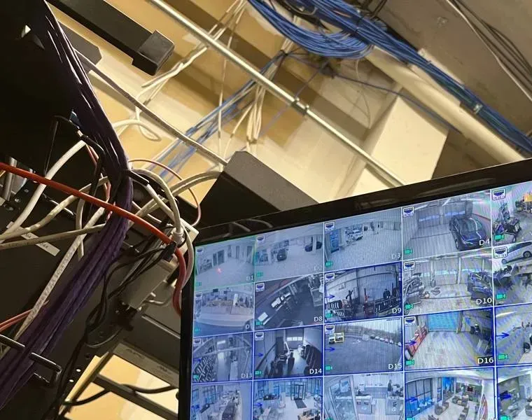 Cable bundles above a wall monitor — Westchester video wall cabling reference Westchester County video wall reference photo: bundles of purple, white and blue cable running along joists above the top edge of a wall monitor showing camera tiles