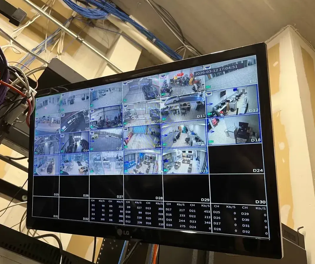 LG monitor under overhead cable runs — Westchester video wall reference Westchester County video wall installation reference photo: an LG wall monitor showing a grid of live camera views and a bitrate table, hung below bundles of blue and white cable in an open ceiling