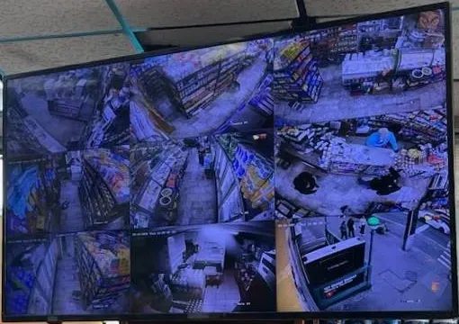 Store display split into eight camera views — Westchester retail display reference Westchester County video wall reference photo: a large flat display in a store showing eight camera views of aisles and a counter, with one tile blurred