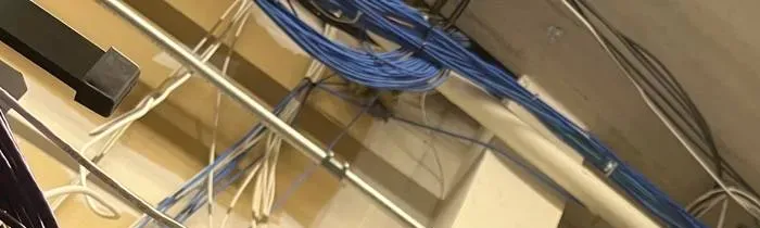 Wireless camera installation NYC reference photo: bundles of blue and white network cables running along a metal pipe and ceiling structure, with a dark bracket at the left edge